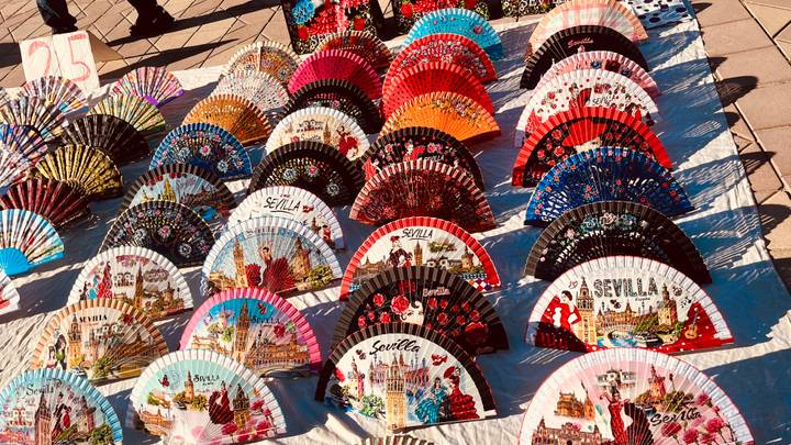 Display of colorful hand fans with Sevilla motifs arranged on a market blanket.