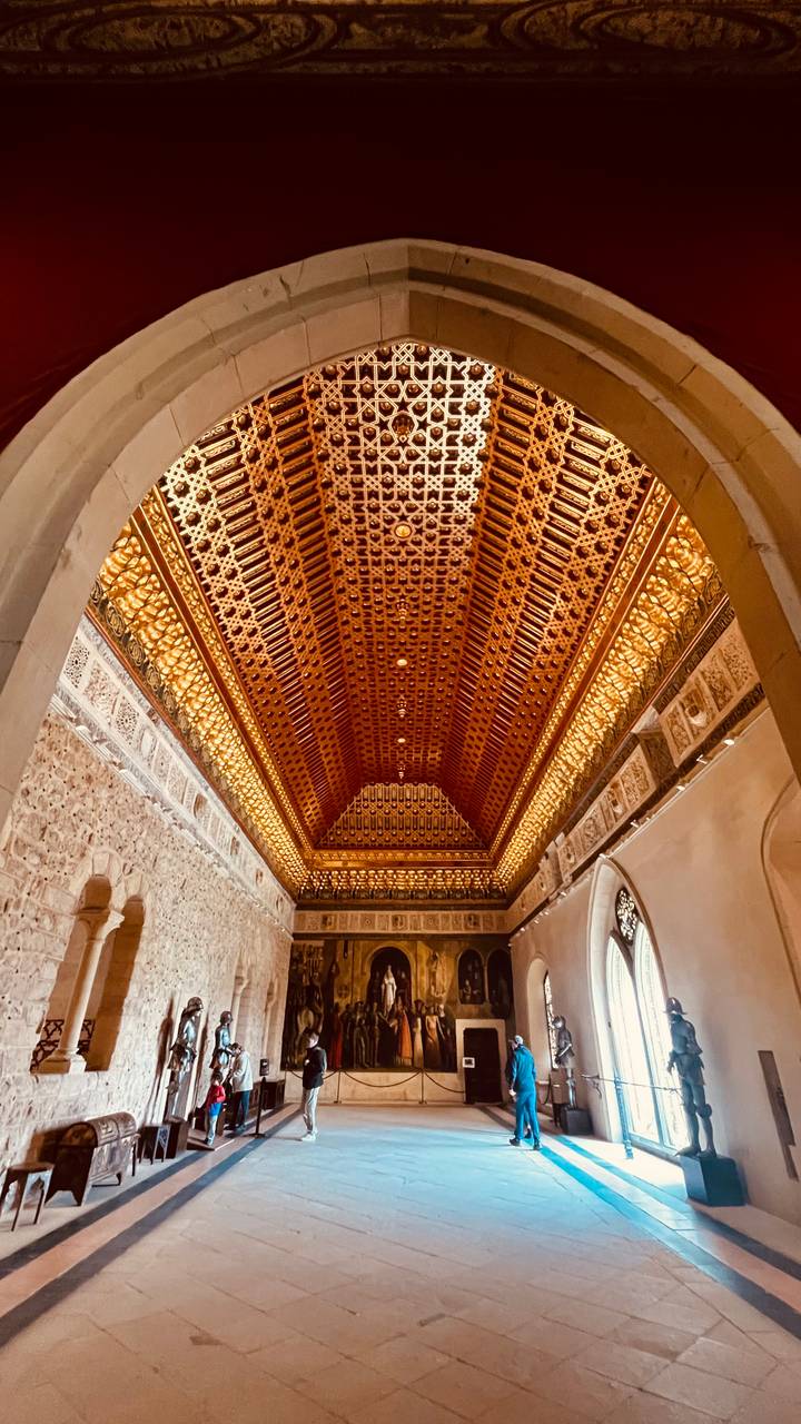 Intricately carved and illuminated wooden ceiling in a historic hall.