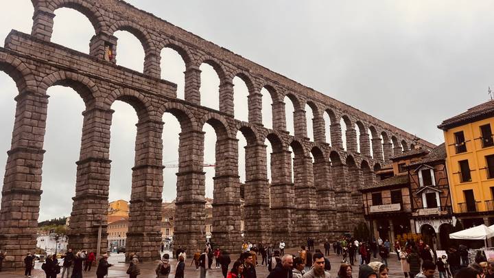 Massive Roman aqueduct stretching across a town square crowded with tourists.
