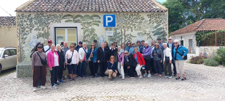 Large tour group poses in front of a quaint Portuguese building with botanical tile art and a parking sign.