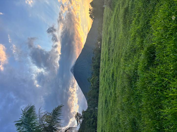 Arenal Volcano rising above green pastureland with dramatic sunset clouds and golden light.