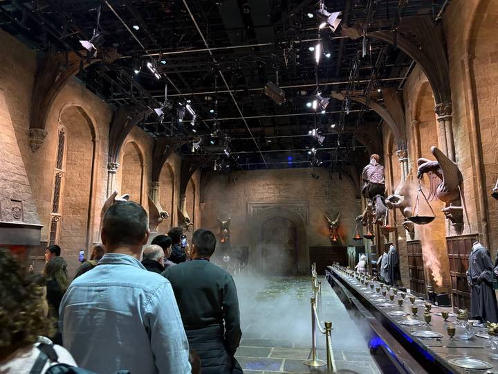 Visitors walking through a mist-filled great hall set with long tables and gargoyles overhead