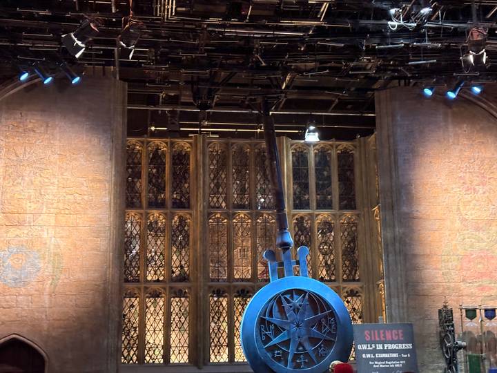 Large blue pendulum prop set against tall stained-glass windows on a studio stage