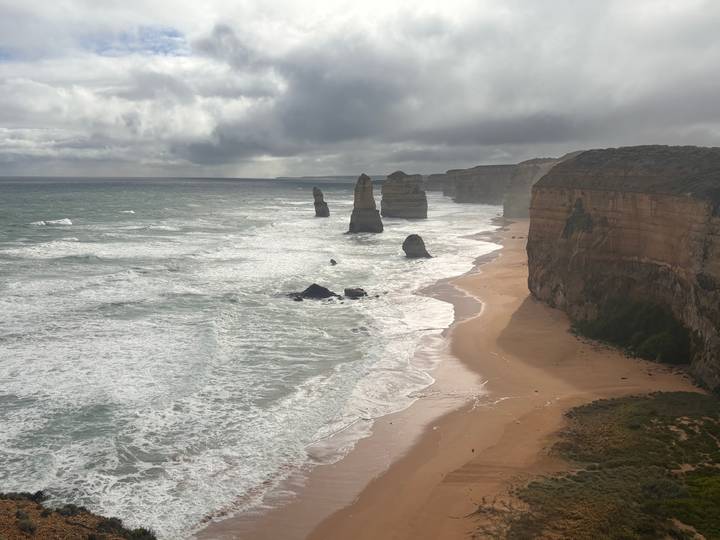Dramatic coastal cliffs and limestone stacks of the Twelve Apostles rising from wild surf under moody clouds