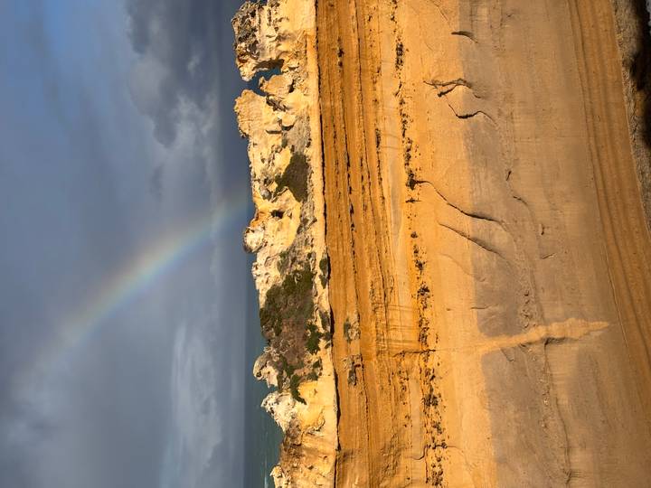 Rainbow arching over rugged orange coastal rock formations lit by low sunlight