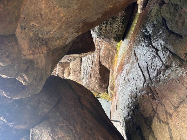 Wet, weathered boulders forming a narrow passage with light filtering through