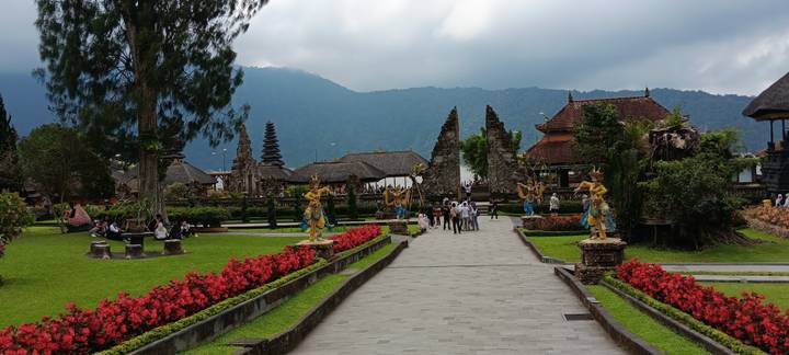 Ornate Balinese temple complex with stone gates, statues and garden path framed by mountains.