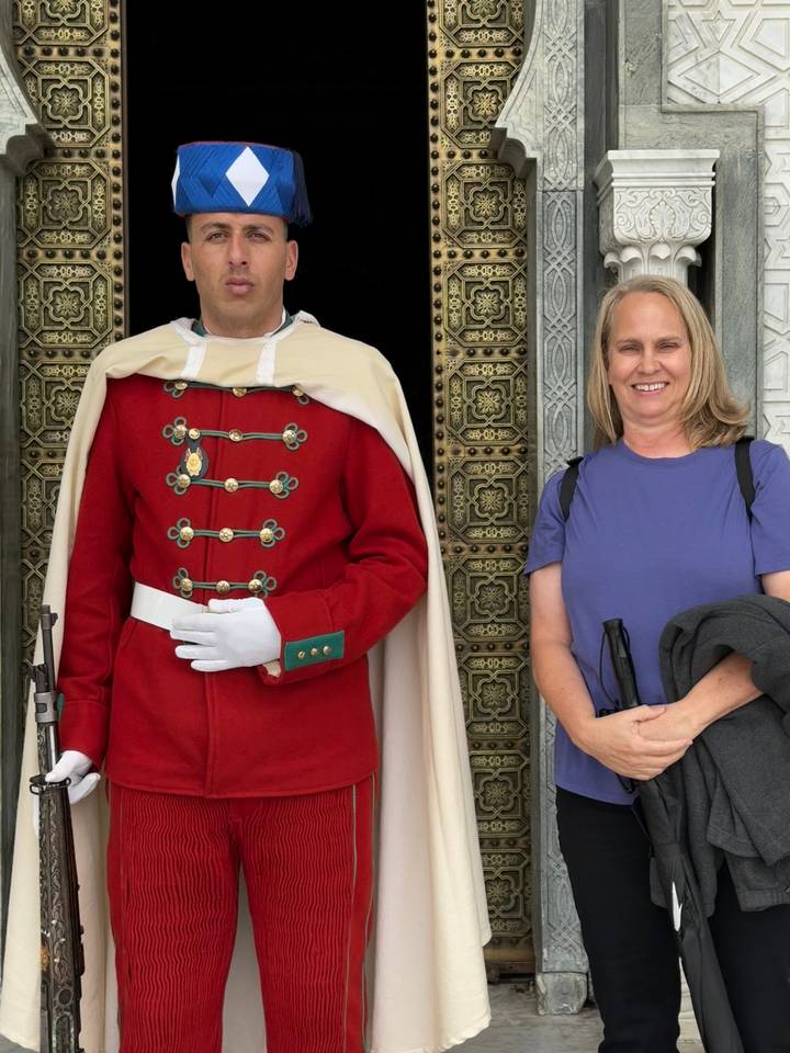 Smiling tourist poses beside a ceremonial guard in red uniform at an ornate bronze doorway.