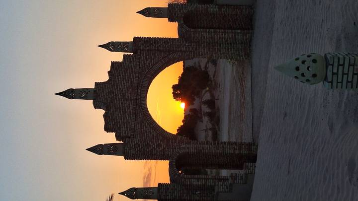 Brick archway framing an orange sun descending over desert dunes.