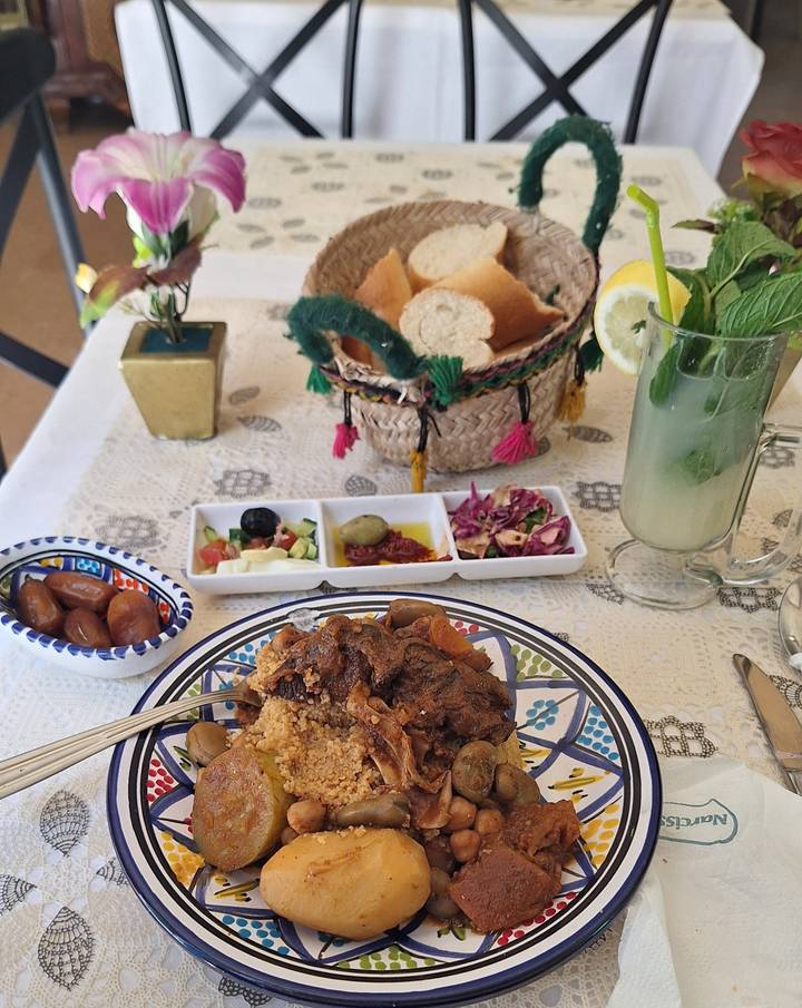 Traditional Tunisian meal of couscous with accompaniments and mint lemonade served on patterned tablecloth.