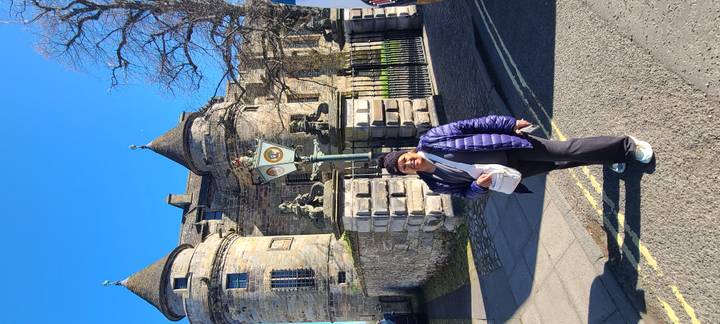 Traveller poses before turrets and stone walls of a Scottish castle on a sunny day.