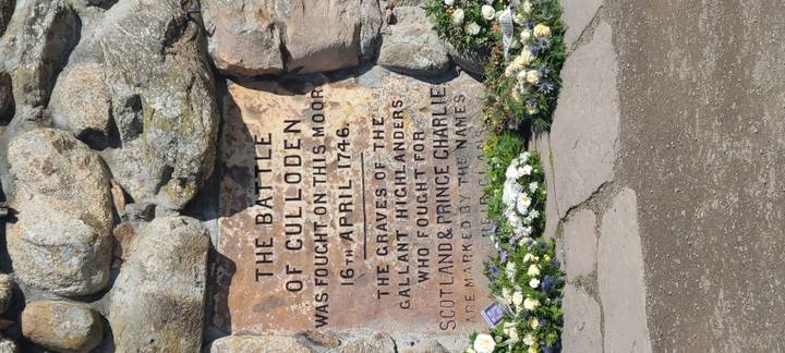 Engraved Culloden Battlefield memorial stone commemorating the 1746 battle surrounded by flowers.