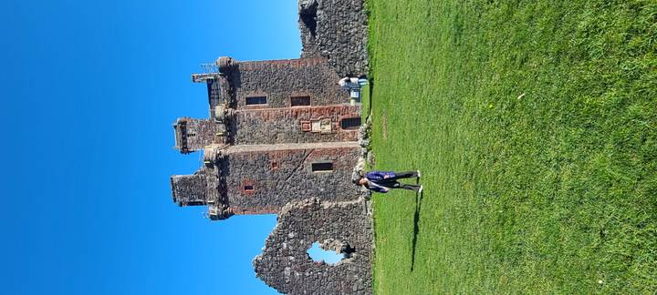 Visitors explore the red-stone ruins of Castle Stalker set on green grass under clear sky.