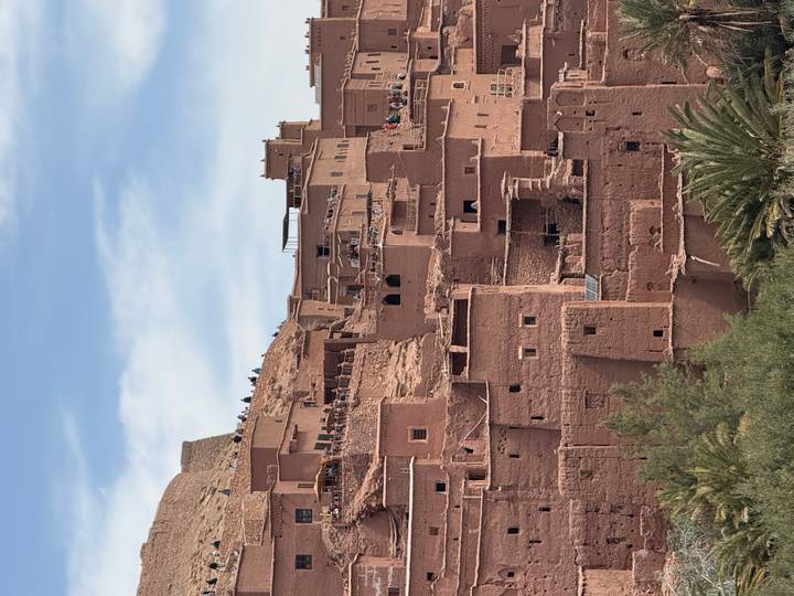 The earthen adobe buildings of Aït Benhaddou cascade down a hillside beneath a blue sky