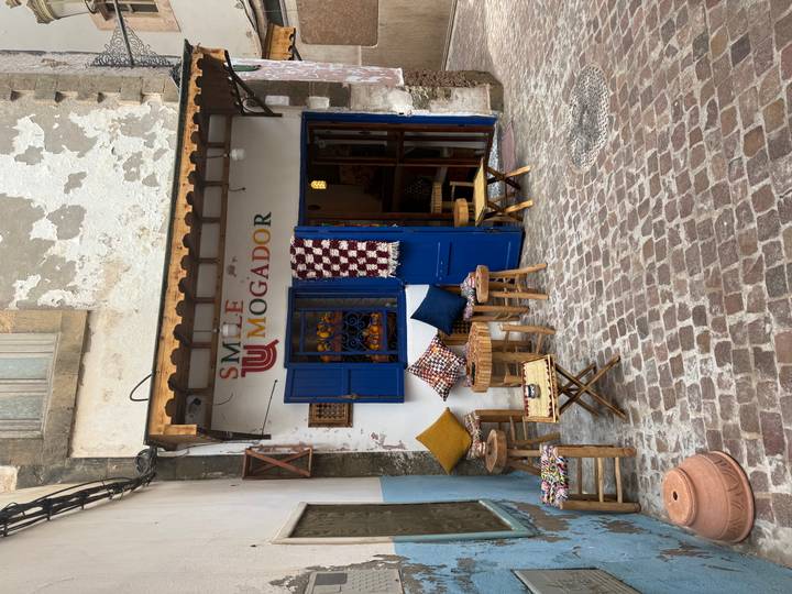 A cozy café with blue doors, patterned cushions and wooden stools brightens a cobbled medina alley