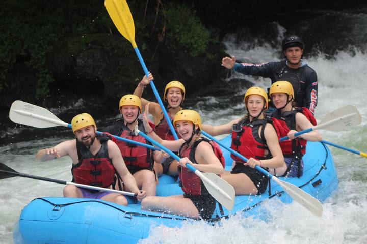 Smiling rafters in a blue inflatable raft paddling through foamy rapids.