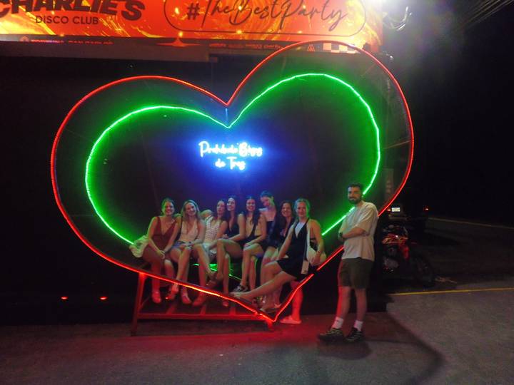Group seated inside a giant neon heart installation glowing brightly at night.