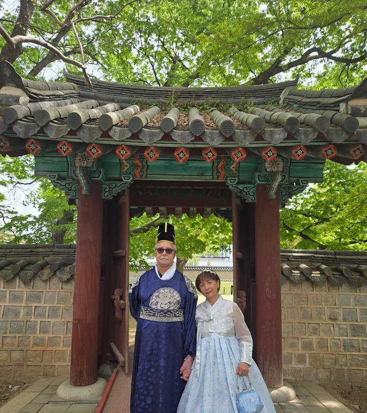 Visitors dressed in traditional Korean attire posing under an ornate wooden gate in a historic courtyard.