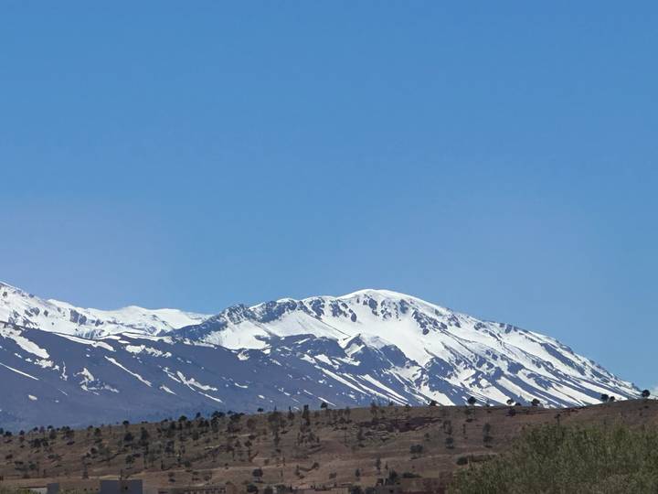 Snow-topped Atlas mountain ridge contrasting against a clear blue sky and arid foreground.