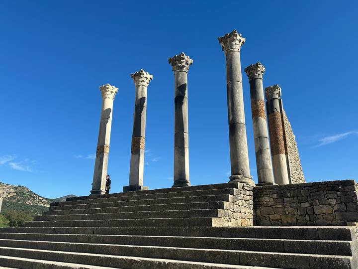 Roman columns of ancient Volubilis rising against a bright blue Moroccan sky.