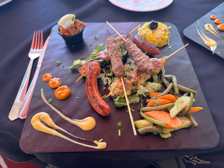 Plate of Moroccan mixed grill skewers with vegetables and colorful sauces arranged artfully.