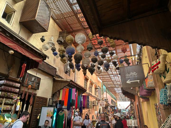 Narrow souk alley in Marrakesh decorated with hanging metal lanterns and colorful textiles.