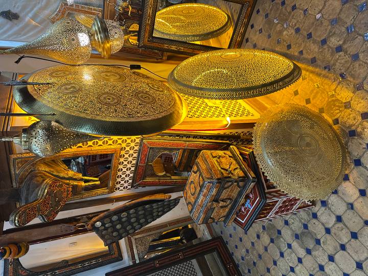 An ornate Moroccan shop interior displaying large hammered-brass trays, lanterns and painted wooden furniture.