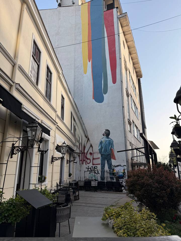 Tall narrow alley with street art of a boy gazing upward toward colorful abstract shapes on a building wall.