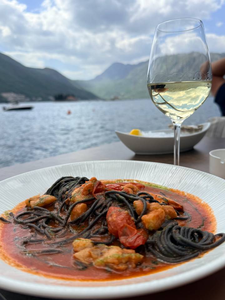 Close-up of seafood pasta in tomato sauce with a glass of white wine overlooking a tranquil bay.