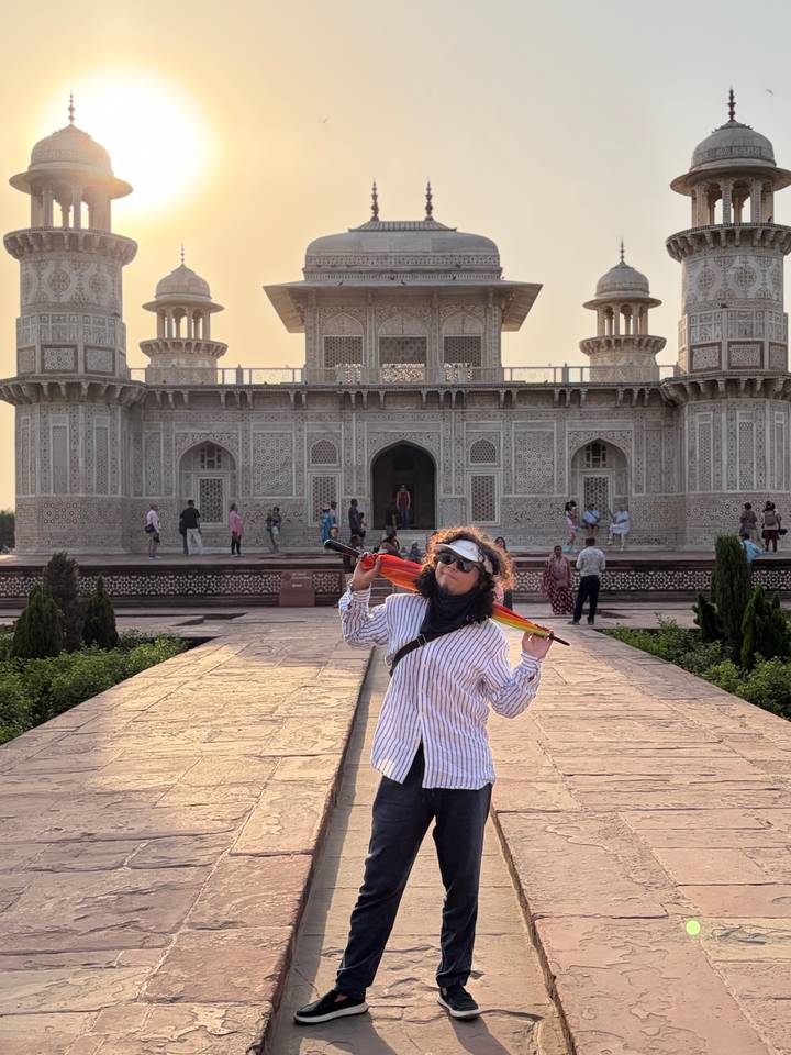 Traveller posing with a colourful umbrella in front of an ornate Mughal-style marble mausoleum courtyard.