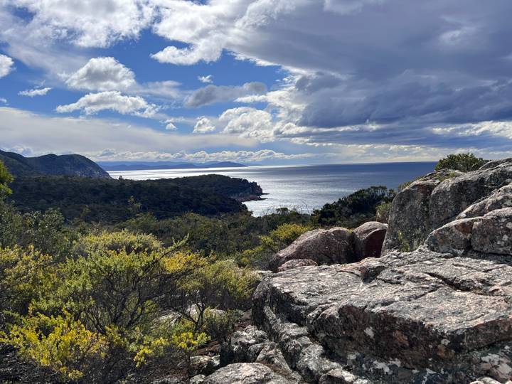 Rocky coastal viewpoint overlooking forests, sea cliffs and sparkling ocean beneath dramatic clouds.