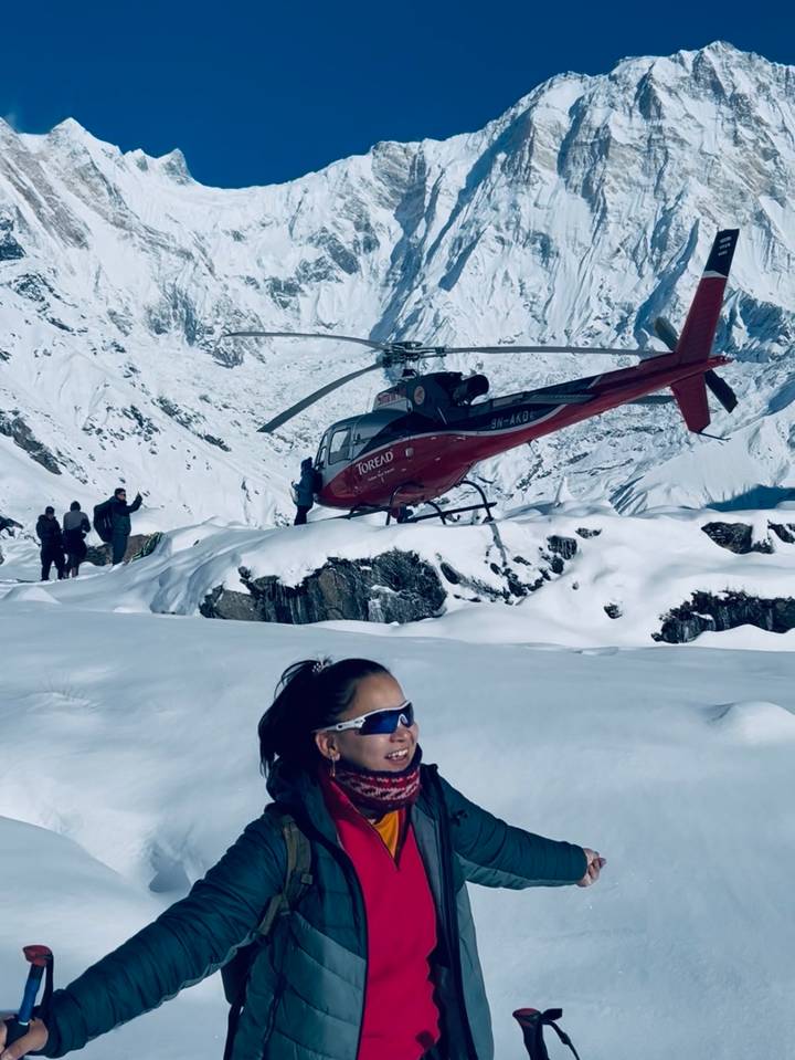 Red rescue helicopter landed on a snowy plateau amid towering Himalayan peaks with trekkers nearby.