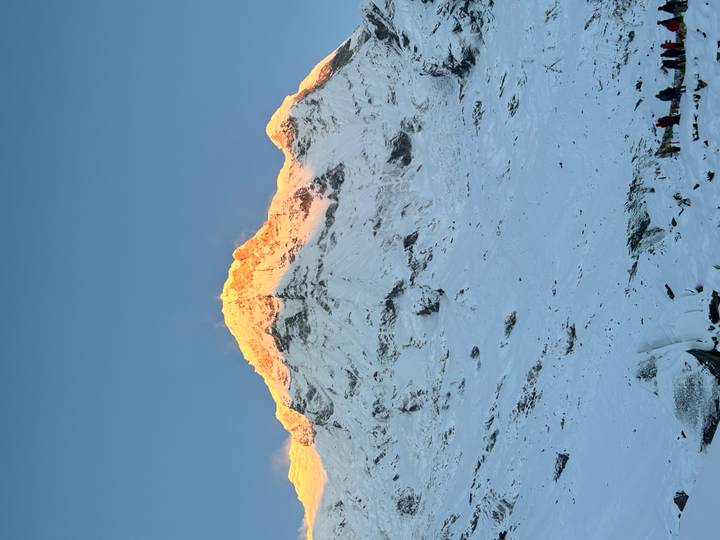 Snow-covered Himalayan summit glowing orange in first light against a clear blue sky.