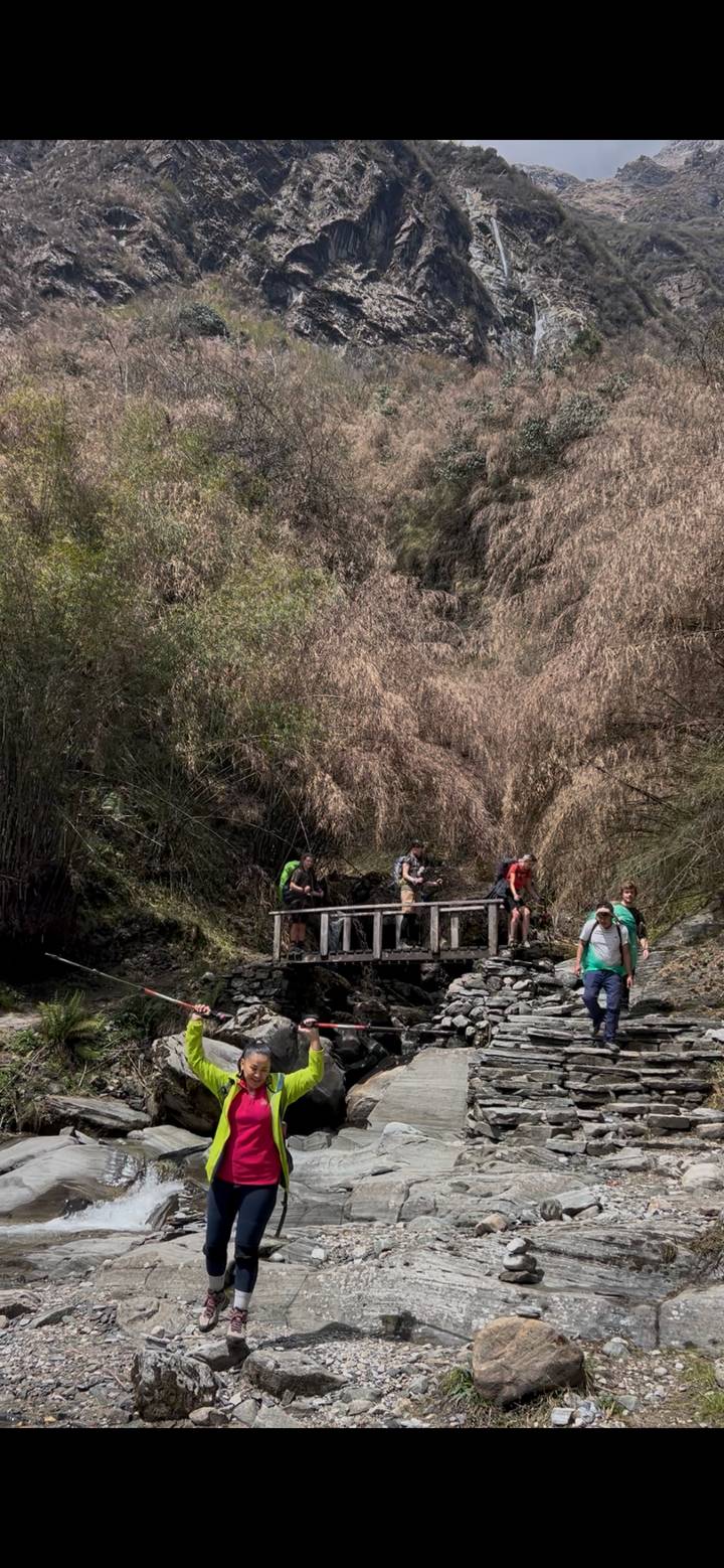 Small group of trekkers crossing a wooden bridge over a rocky stream in a dense valley forest.