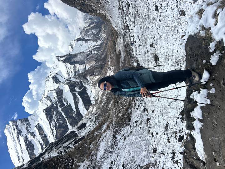 Woman hiker wearing sunglasses stands on snowy valley trail with dramatic jagged peaks behind.