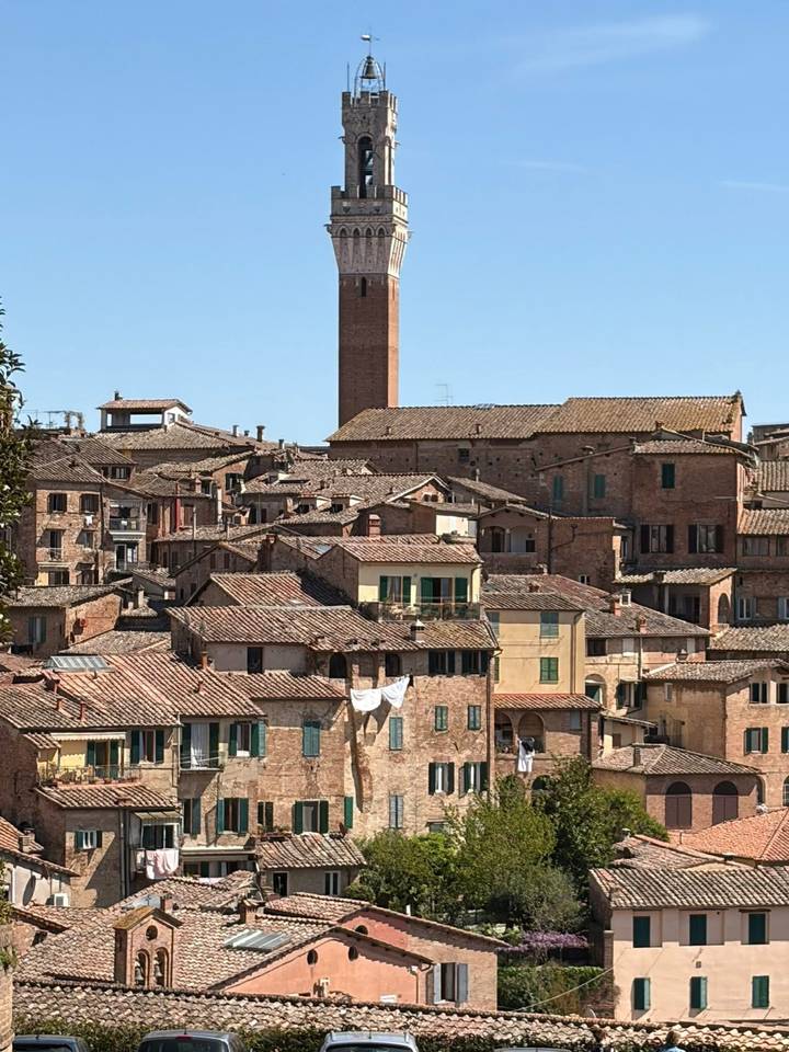 Terracotta rooftops and brick towers of a medieval Italian city under a clear blue sky.