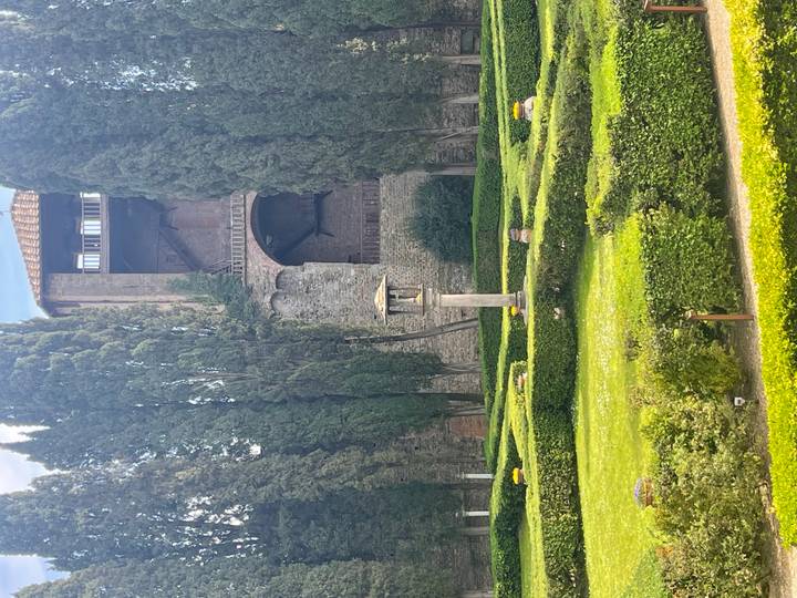 Manicured hedge garden with cypress trees and a historic stone building backdrop.