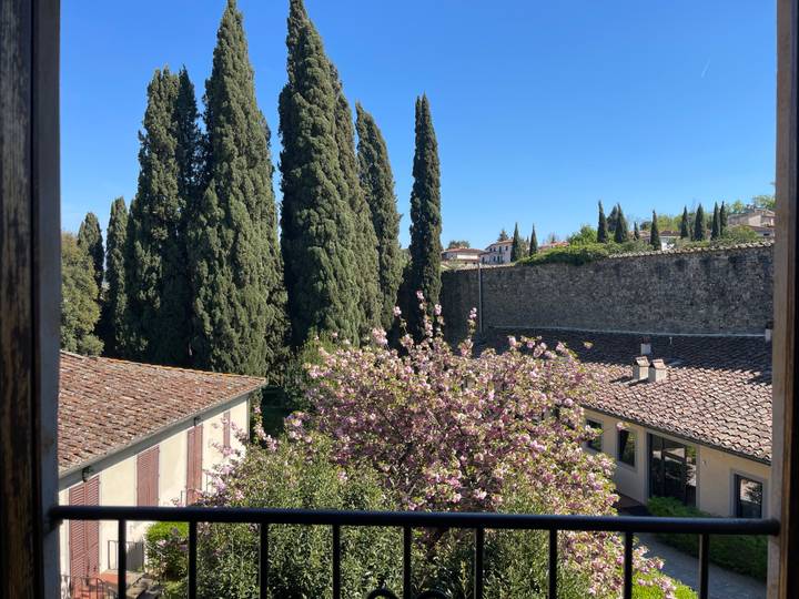 View through a window of spring blossoms, tall cypress trees and stone ramparts under a blue sky.