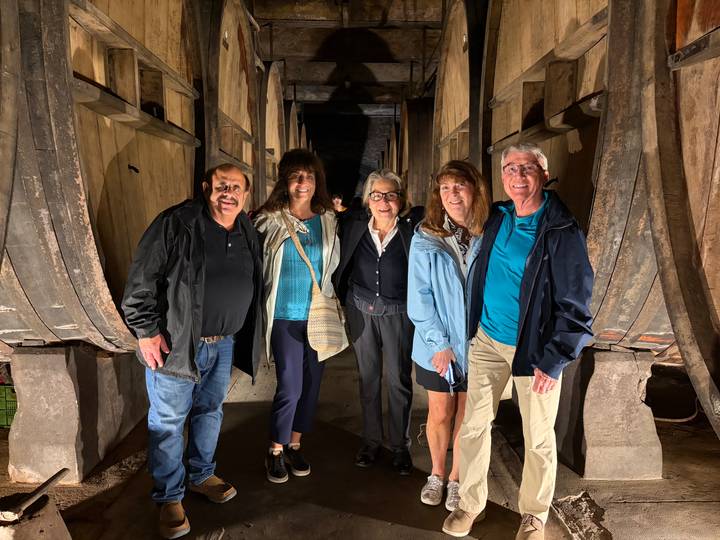 Group of travellers smiling inside a dimly lit historic wine barrel cellar.