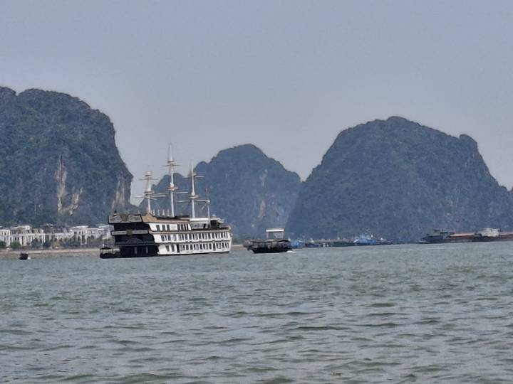 Cruise ship and small boats sail among towering limestone karst islands in a hazy bay.