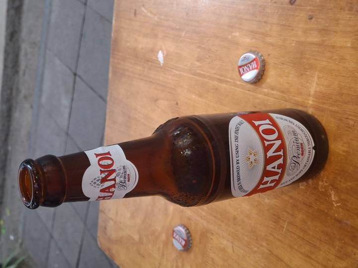 Close-up of a Hanoi Premium beer bottle on a wooden table with the bottle cap lying nearby.