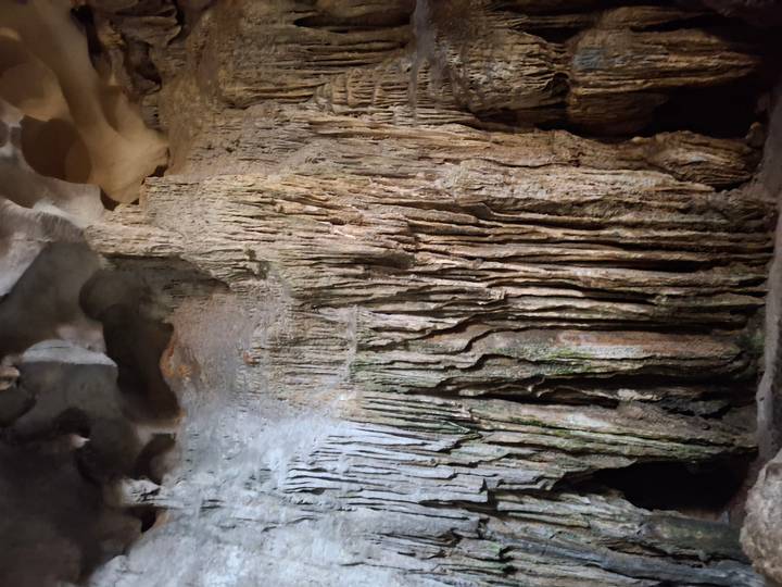 Detailed limestone stalactites and flowstone formations inside a dimly lit cave chamber.