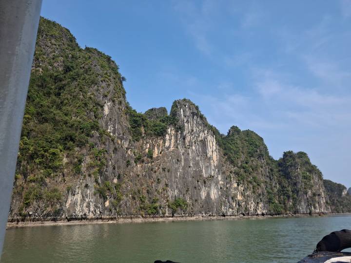 Dramatic limestone karst cliffs rising from turquoise waters under a clear blue sky.