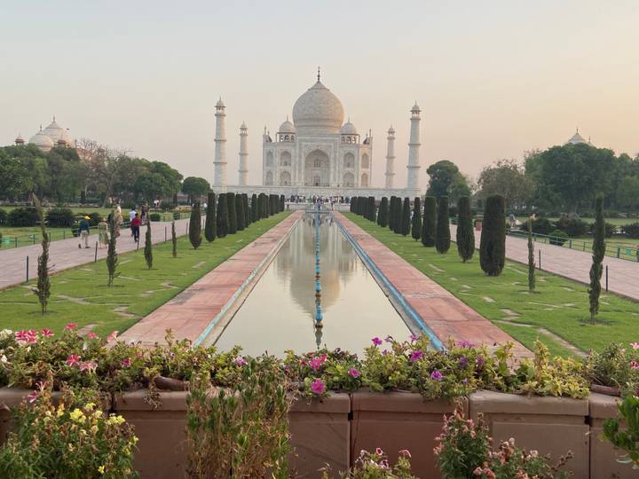 Iconic frontal view of the Taj Mahal reflected in its long water channel at sunset light.