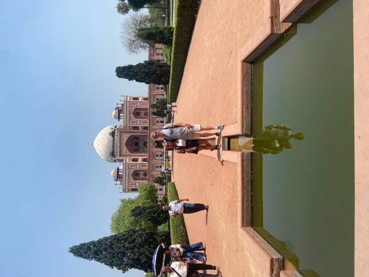 Couple standing in front of Humayun's Tomb with symmetrical Mughal gardens and clear blue sky.
