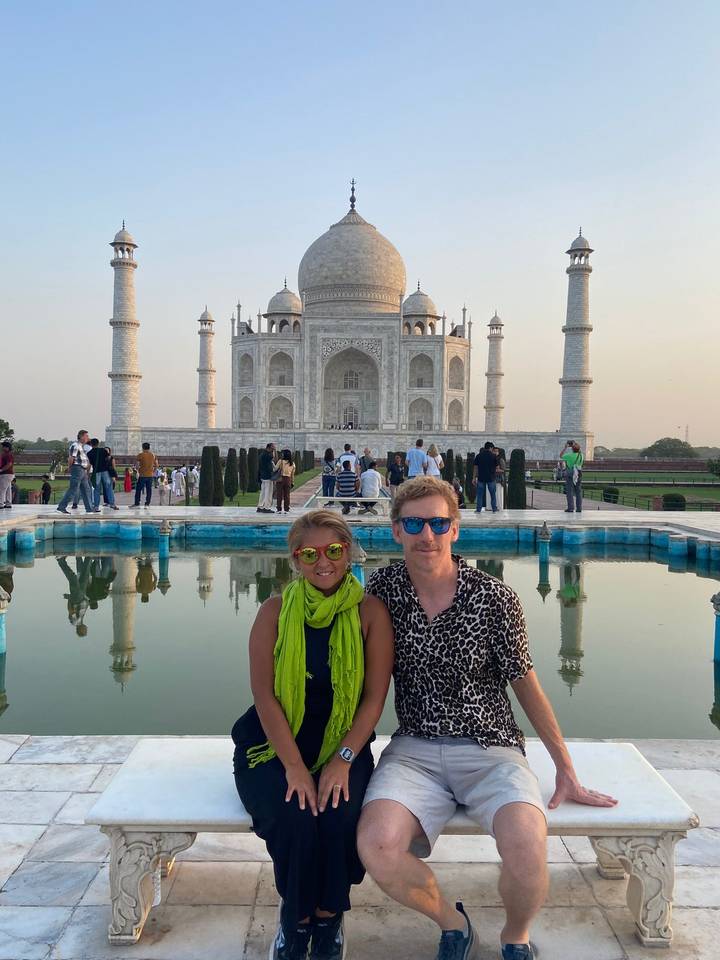 Couple seated beside a reflecting pool with the Taj Mahal rising majestically behind them at dusk.