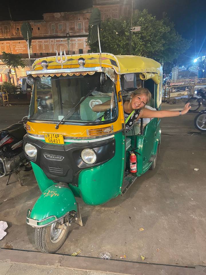 Traveler enthusiastically leaning out of a green auto-rickshaw on a busy night street.