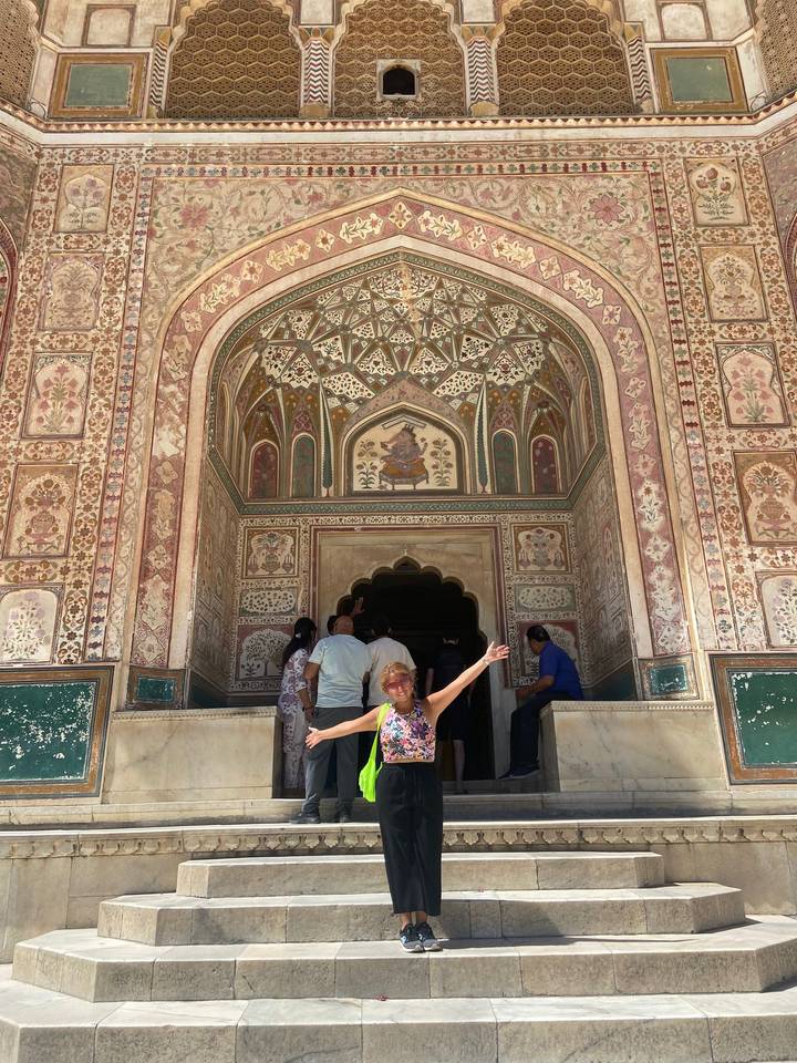 Traveler spreads arms joyfully in front of the ornate painted Ganesh Pol gate at Amber Fort.