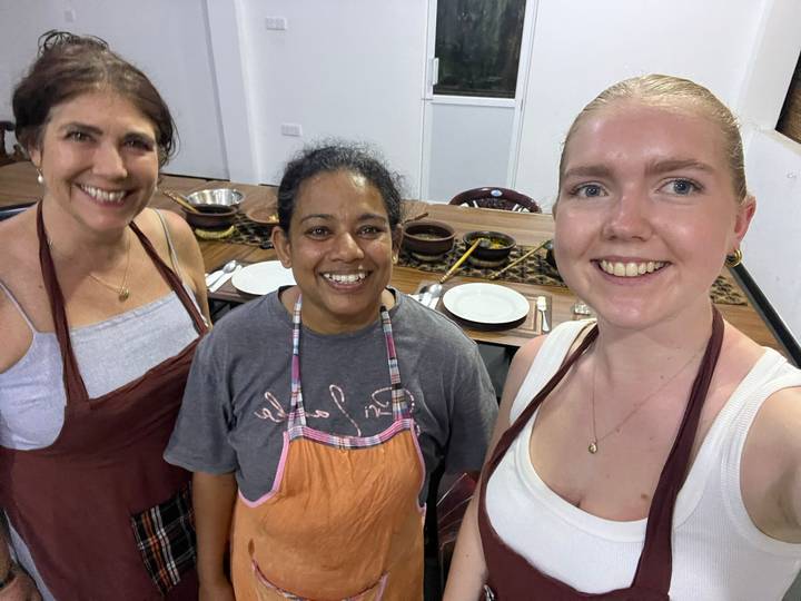 Cooking class selfie with instructor and two participants wearing aprons inside a kitchen classroom.