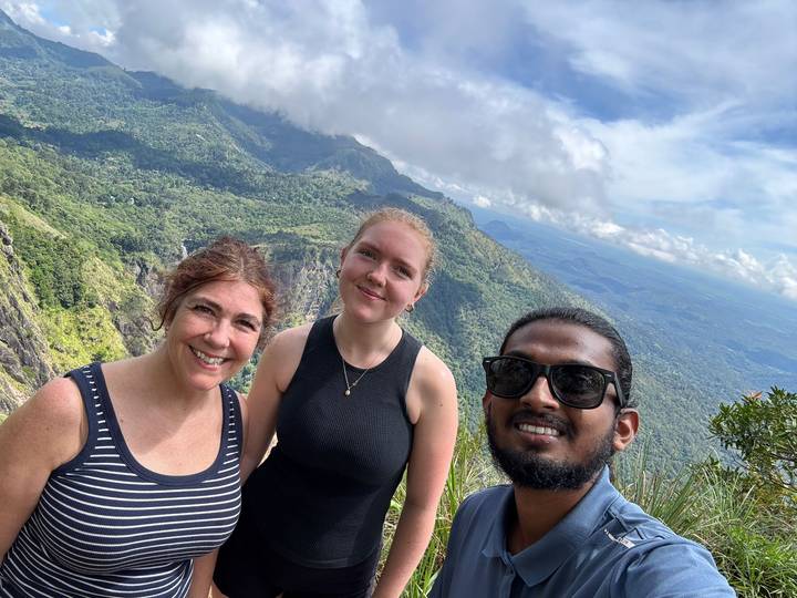 Selfie of three hikers on a mountain ridge with sweeping forested valleys stretching behind.